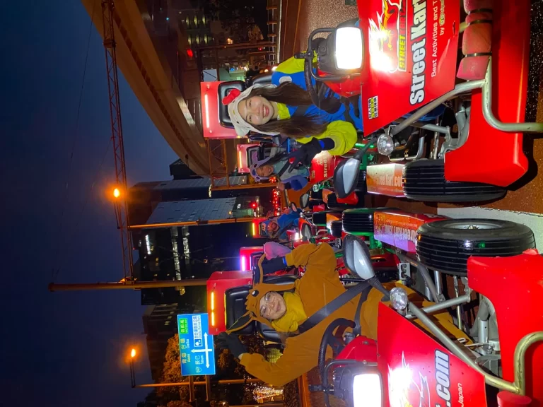 Riders in bright jackets on red mini tractors lined up along a city street at night in a parade.